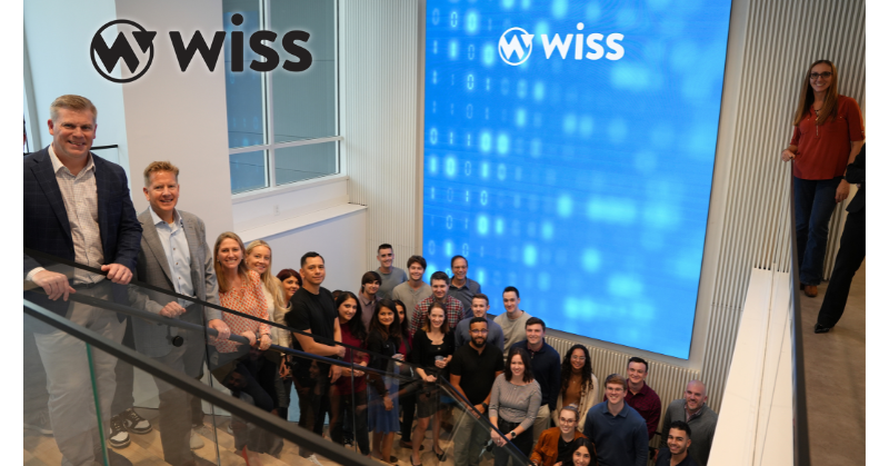 Wiss team members gathered on a modern staircase in front of a large digital screen displaying the Wiss logo, celebrating their recognition as a 2025 Top 50 CAS Practice.