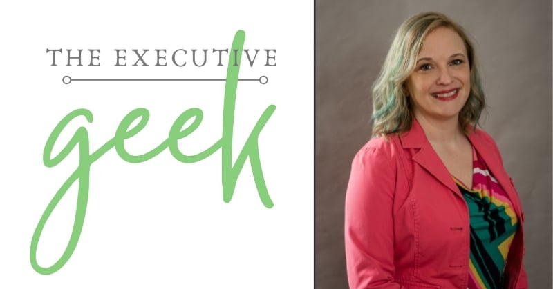 Logo for The Executive Geek alongside a headshot of Heather S. Kwitschau, who is smiling and wearing a bright pink jacket over a colorful top.