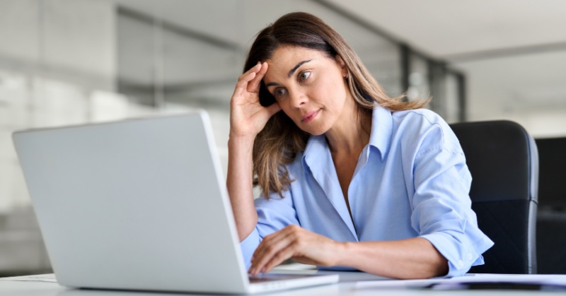 Accounting professional looking concerned while working on a laptop at a desk in a modern office.
