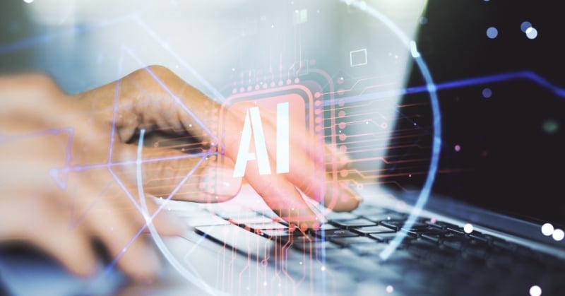 Close-up of a person's hands typing on a laptop keyboard, overlaid with digital graphics and the letters "AI," symbolizing artificial intelligence technology in use.
