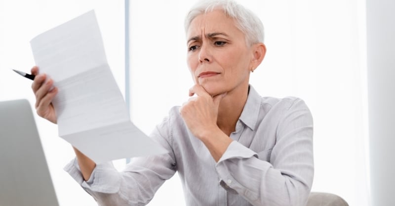 Businesswoman reviewing paperwork with a concerned expression while seated at a desk with a laptop, illustrating unexpected sales tax exposure and financial compliance concerns.