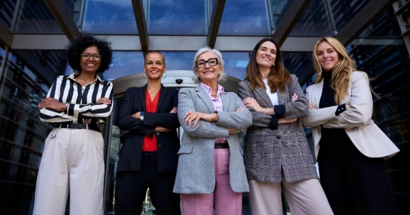 Group of confident businesswomen standing together outside a modern office building, symbolizing feminine leadership and diversity in accounting.