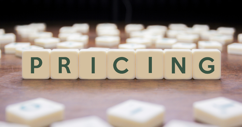 The word “PRICING” spelled out with Scrabble-style letter tiles on a wooden table, surrounded by scattered tiles in the background.