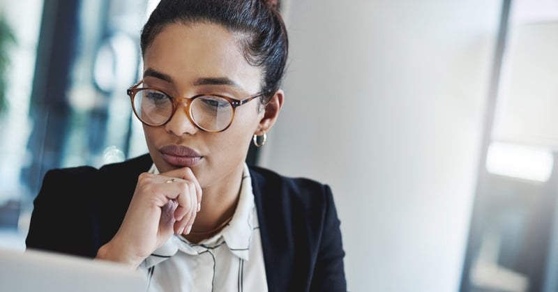 Business professional wearing glasses looking thoughtfully at a computer screen while reviewing financial information.