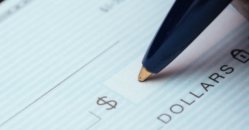 Close-up of a pen filling out the dollar amount on a paper check, symbolizing traditional payment methods being phased out.