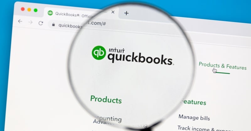 Close-up of the Intuit QuickBooks website homepage with a magnifying glass highlighting the QuickBooks logo and navigation links for Products & Features.