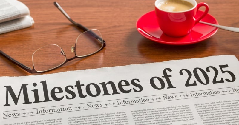 Newspaper headline reading “Milestones of 2025” on a desk with reading glasses and a red coffee cup.