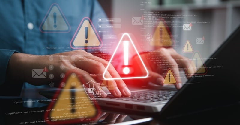Hands typing on a laptop with cybersecurity warning icons and alert symbols overlayed, representing a data breach.