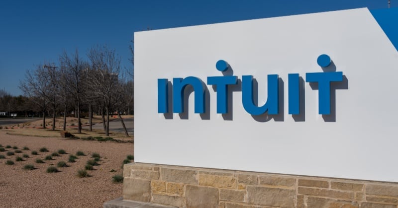 Intuit logo on a large white outdoor sign at the company’s campus, with a desert landscape and leafless trees in the background under a clear blue sky.