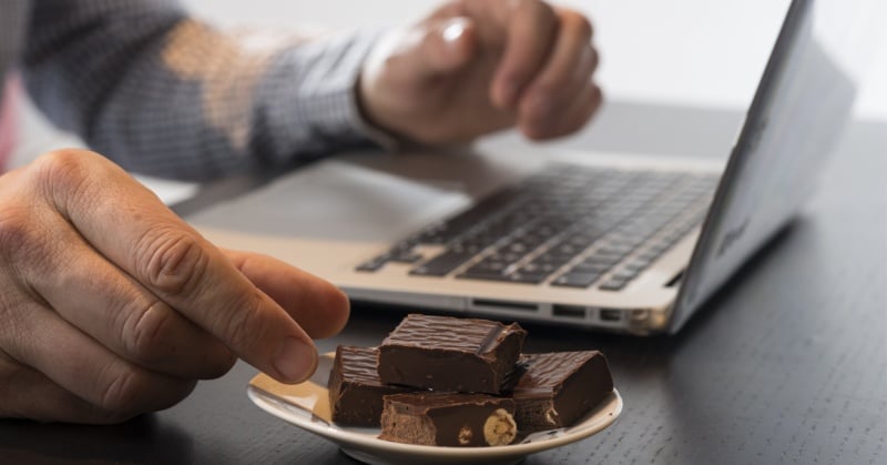 Person working on a laptop with a small plate of chocolate candy bars on a desk.