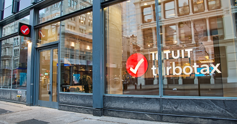 Exterior of an Intuit TurboTax retail storefront with large glass windows and the TurboTax logo visible from the sidewalk.