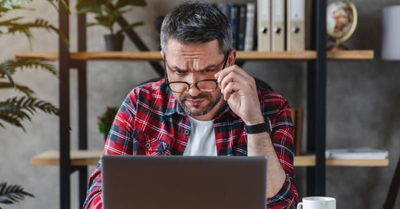 Man wearing glasses looking concerned while working on a laptop at a desk, reviewing financial or accounting data.