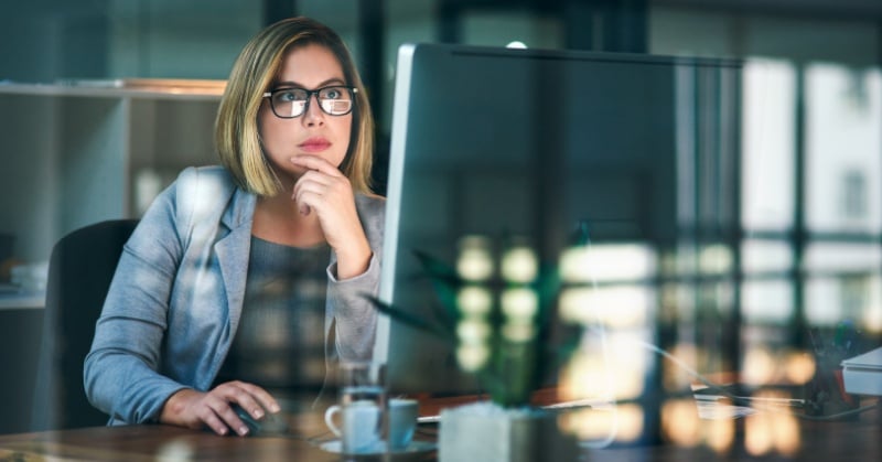 “A focused business professional working at a desktop computer in a modern office, thoughtfully analyzing information on the screen.