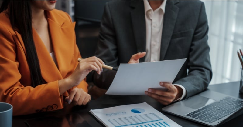 Two professionals reviewing financial documents and charts during a business meeting