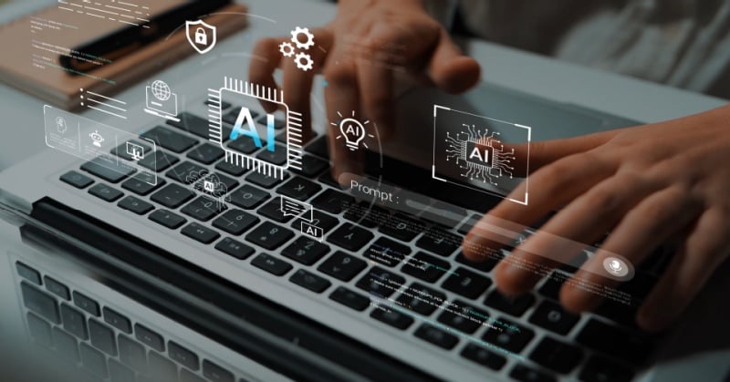 Close-up of hands typing on a laptop keyboard with a transparent digital overlay showing AI-related icons, including a microchip labeled “AI,” data symbols, security icons, and interface elements, suggesting artificial intelligence technology and automation.