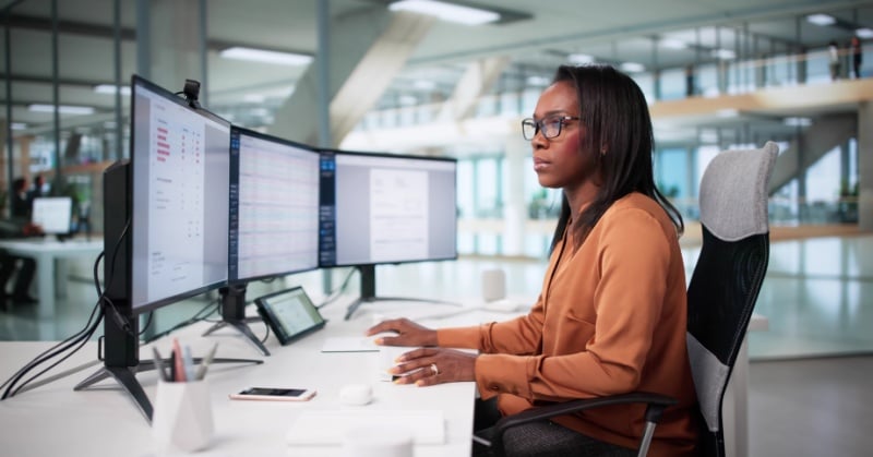 Accounting professional working at a dual-monitor workstation reviewing financial data dashboards in a modern office setting.