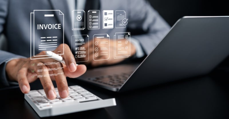 Close-up of a professional using a calculator and laptop with digital invoice and billing icons overlaid on the screen.