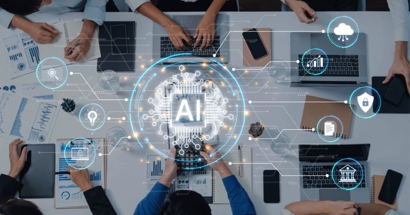 A top-down view of a business meeting table with people using laptops, tablets, and paperwork, overlaid with a glowing AI graphic at the center and connected digital icons representing cloud computing, analytics, security, and finance.