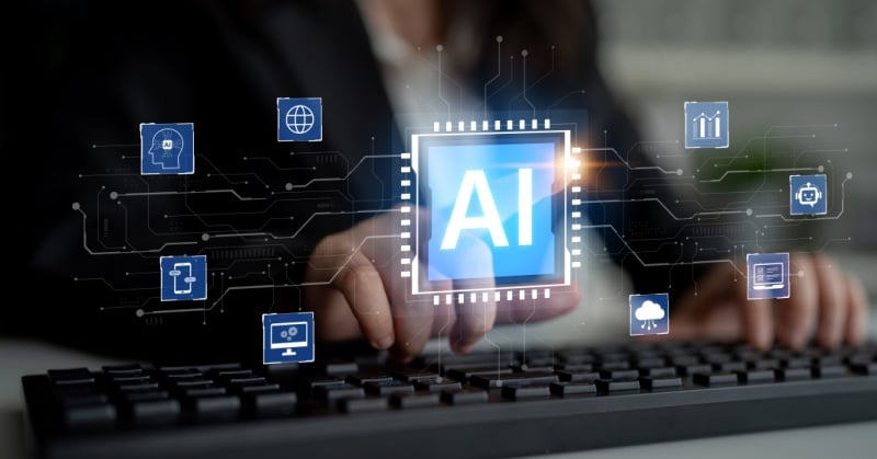 Business professional typing on a keyboard with a glowing AI interface superimposed above the keys, surrounded by floating technology icons representing data, automation, analytics, cloud computing, and digital tools.