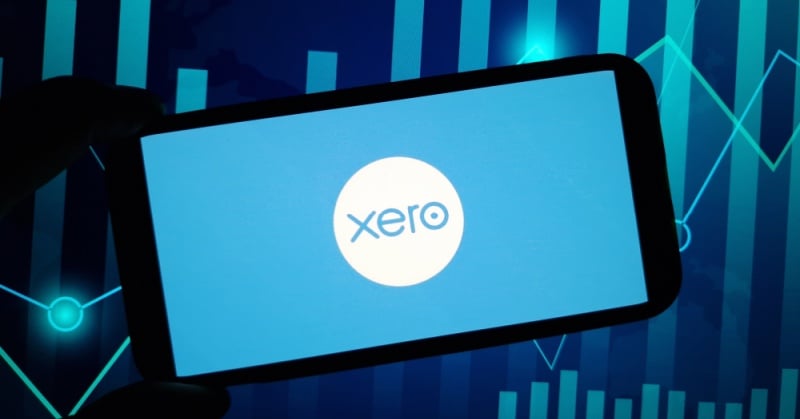 Xero logo displayed on a smartphone screen against a blue financial chart background, representing accounting technology and business data analytics.