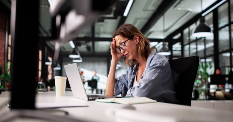 Stressed accounting professional working at a laptop in a modern office while managing manual firm workflows.