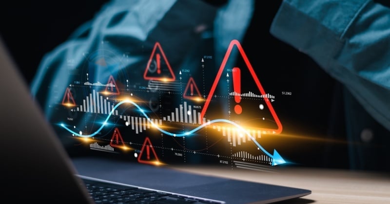 A person at a desk reviewing financial data on a laptop, with digital warning symbols and fluctuating graphs overlaid, symbolizing business risks and red flags in financial systems.
