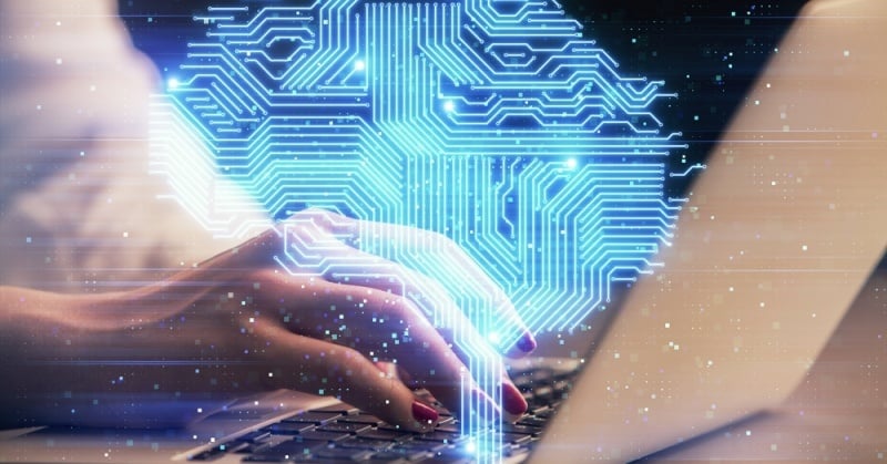 Close-up of a person's hand typing on a laptop keyboard with a glowing blue digital brain overlay, symbolizing artificial intelligence and machine learning technology integration in professional workflows.