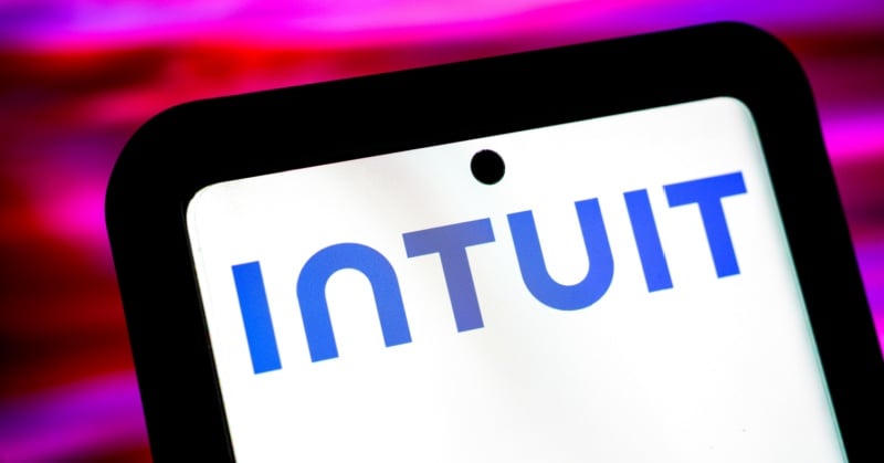 Close-up of an Intuit logo displayed on a smartphone screen with a bright pink and purple blurred background.