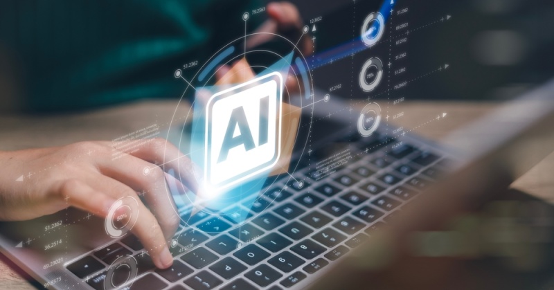 Person using laptop with glowing AI icon and digital data graphics overlay, representing artificial intelligence technology in business applications.