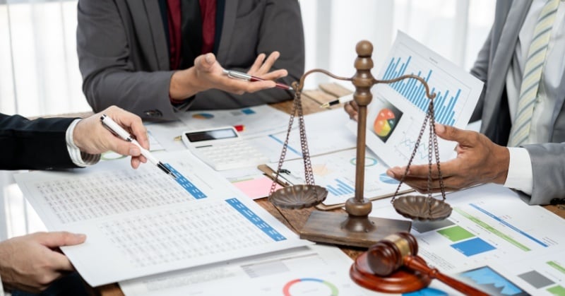 Legal and accounting professionals review financial reports with scales of justice and a gavel on the table.