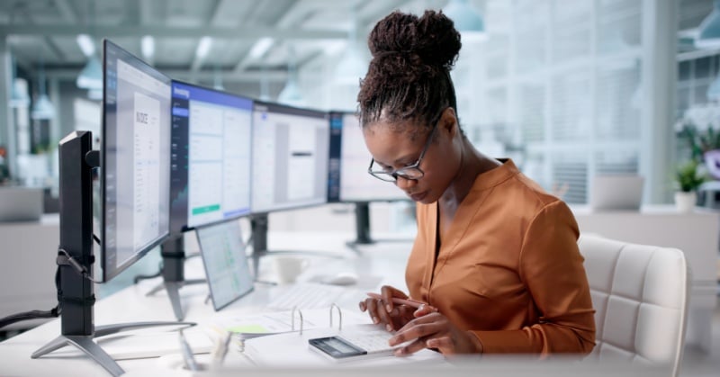 Bookkeeping professional working at a desk with multiple monitors while using a calculator.