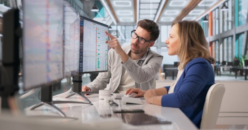Two professionals reviewing accounting data and workflow dashboards on office monitors.