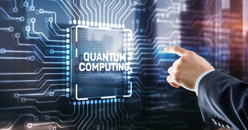 Businessperson pointing at a digital chip labeled “Quantum Computing” over a circuit board background.
