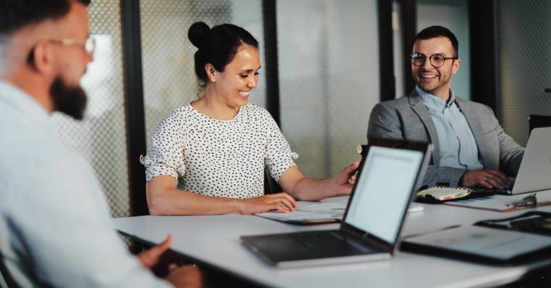 Three accounting professionals collaborate around a conference table with laptops and documents in a modern office.