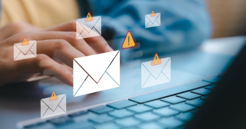 Hands typing on a laptop with floating email icons and warning symbols representing phishing and email security threats.