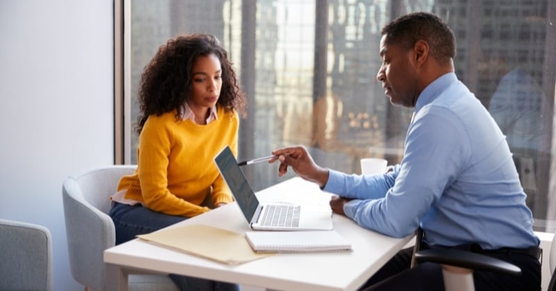 Two accounting professionals discuss financial information on a laptop during a client advisory meeting.