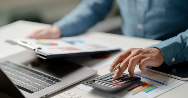 Hands using a calculator beside a laptop and financial reports with charts, representing client sales tax planning.
