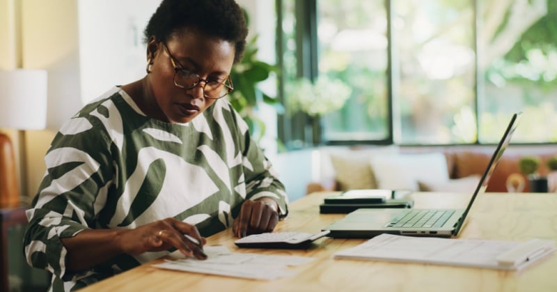 A professional reviewing financial documents at a table with a laptop, supporting small accounting firm planning and advisory work.