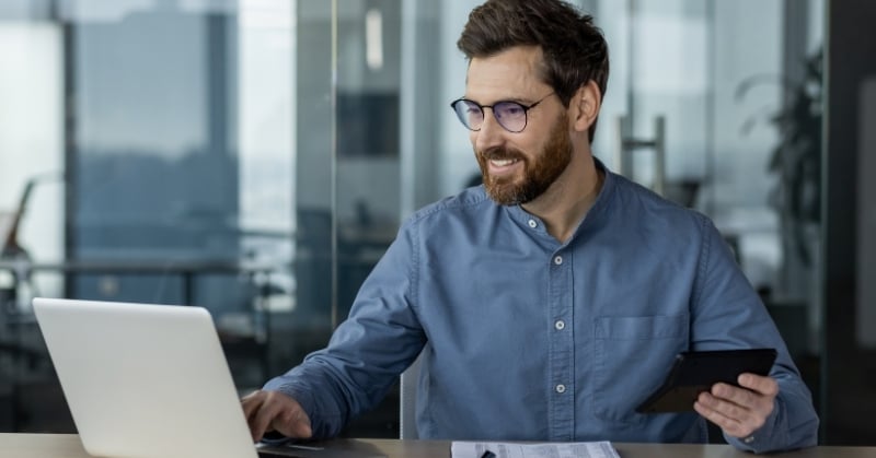 Accounting professional using a laptop and tablet to manage a month-end close process.
