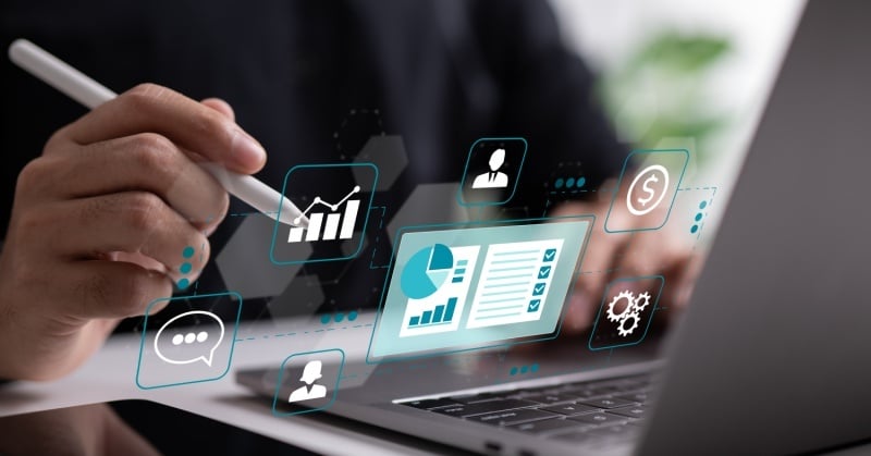 Person using a stylus while working on a laptop, with floating digital icons representing data analytics, user profiles, chat, financial information, and workflow automation, symbolizing digital transformation and smart intake processes in a professional setting.