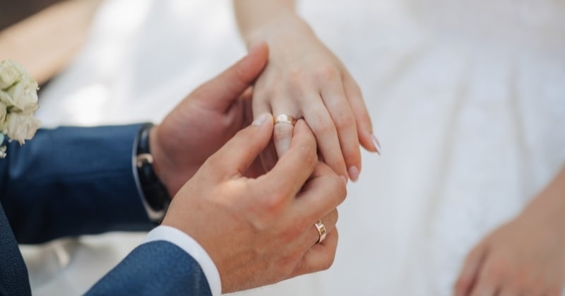 Close-up of a groom placing a wedding ring on a bride’s finger during a wedding ceremony.