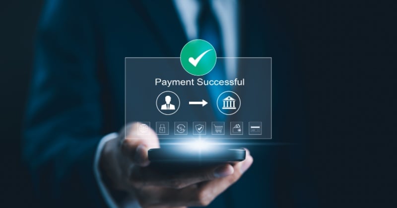 A person in a suit holding a smartphone, with a digital overlay showing a checkmark and the text “Payment Successful,” along with icons representing secure transactions and money transfer to a bank.