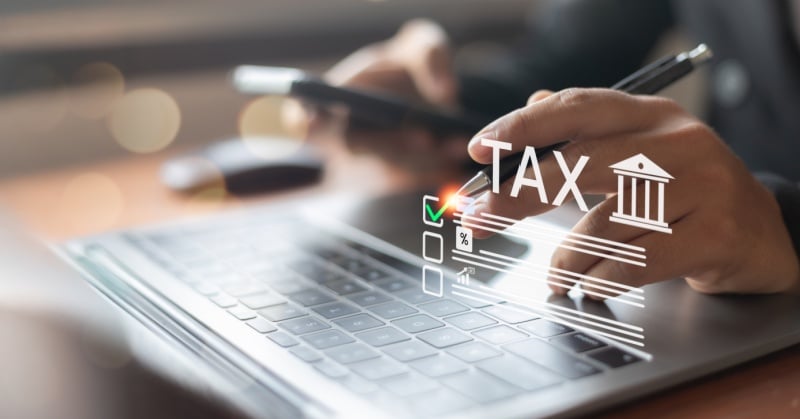 Person using a laptop and smartphone with a stylized “TAX” graphic overlay, representing digital tax filing or online tax workflow solutions.
