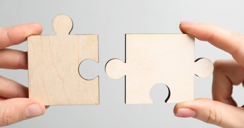 Hands holding two wooden puzzle pieces, representing Accrual’s acquisition of Puzzle and the integration of accounting technology.