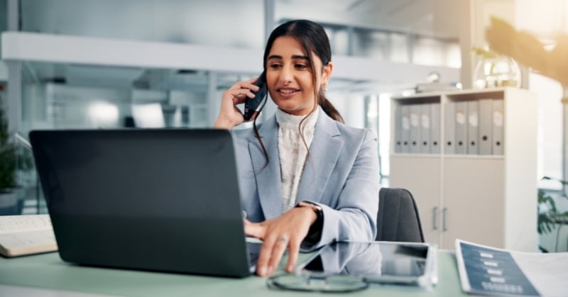 Accounting professional speaking with a client by phone while working on a laptop in a modern office.