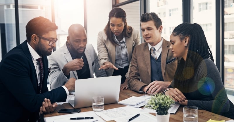 Five professionals gather around a laptop during a collaborative business meeting in a modern office.