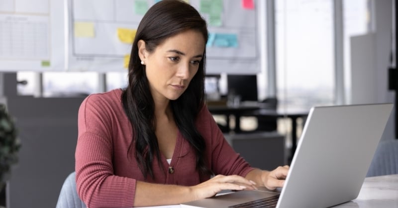 Accounting professional working on a laptop while reviewing financial information in an office.