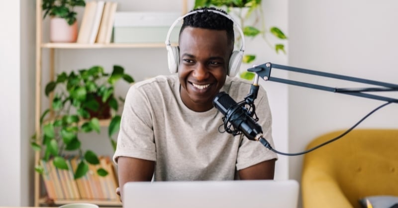 Content creator wearing headphones and speaking into a microphone while working on a laptop in a home office.