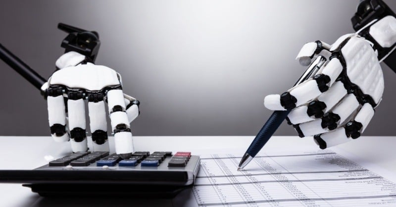 Robot hand using a calculator and pen to verify a report symbolizing the use AI in accounting
