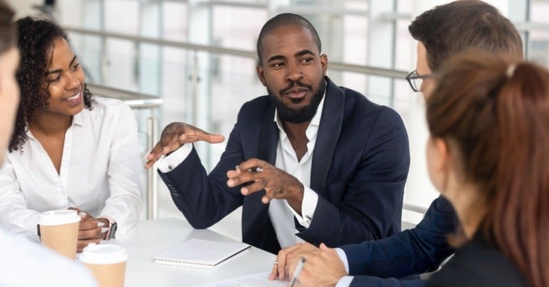 Group of diverse professionals discussing client needs and communication strategies at a meeting table.